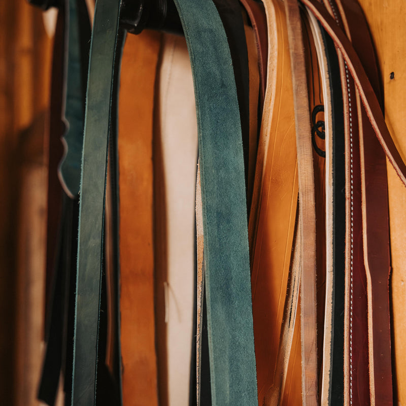 Collection of leather belts hanging on a rack with a wooden background
